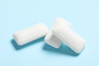 Photo of Tasty white chewing gums on light blue background, closeup