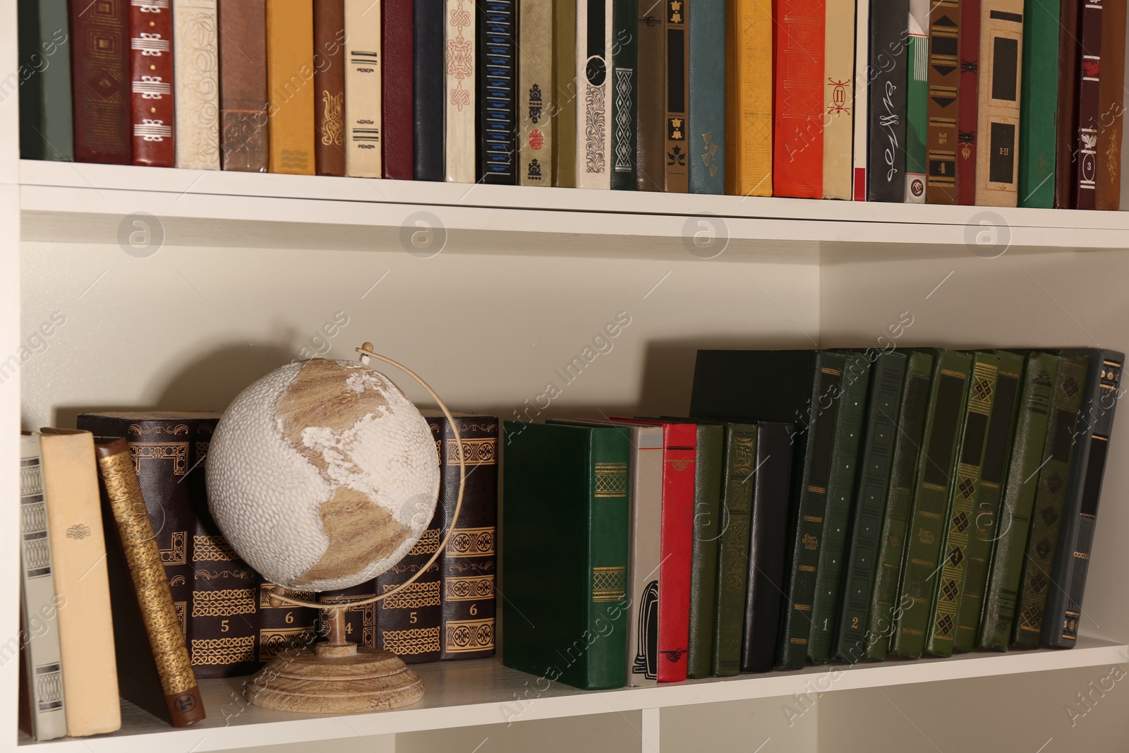 Photo of Collection of different books and decorative elements on shelves in home library