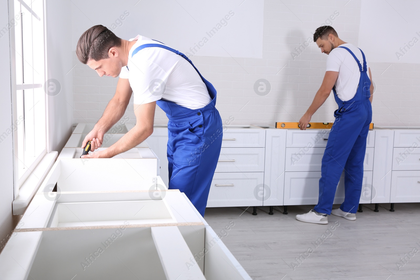 Photo of Workers installing new stylish furniture in kitchen