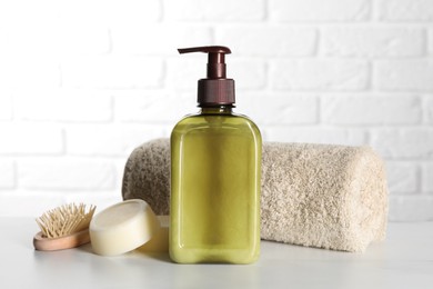 Photo of Bottle of shampoo, terry towel and wooden brush on white table