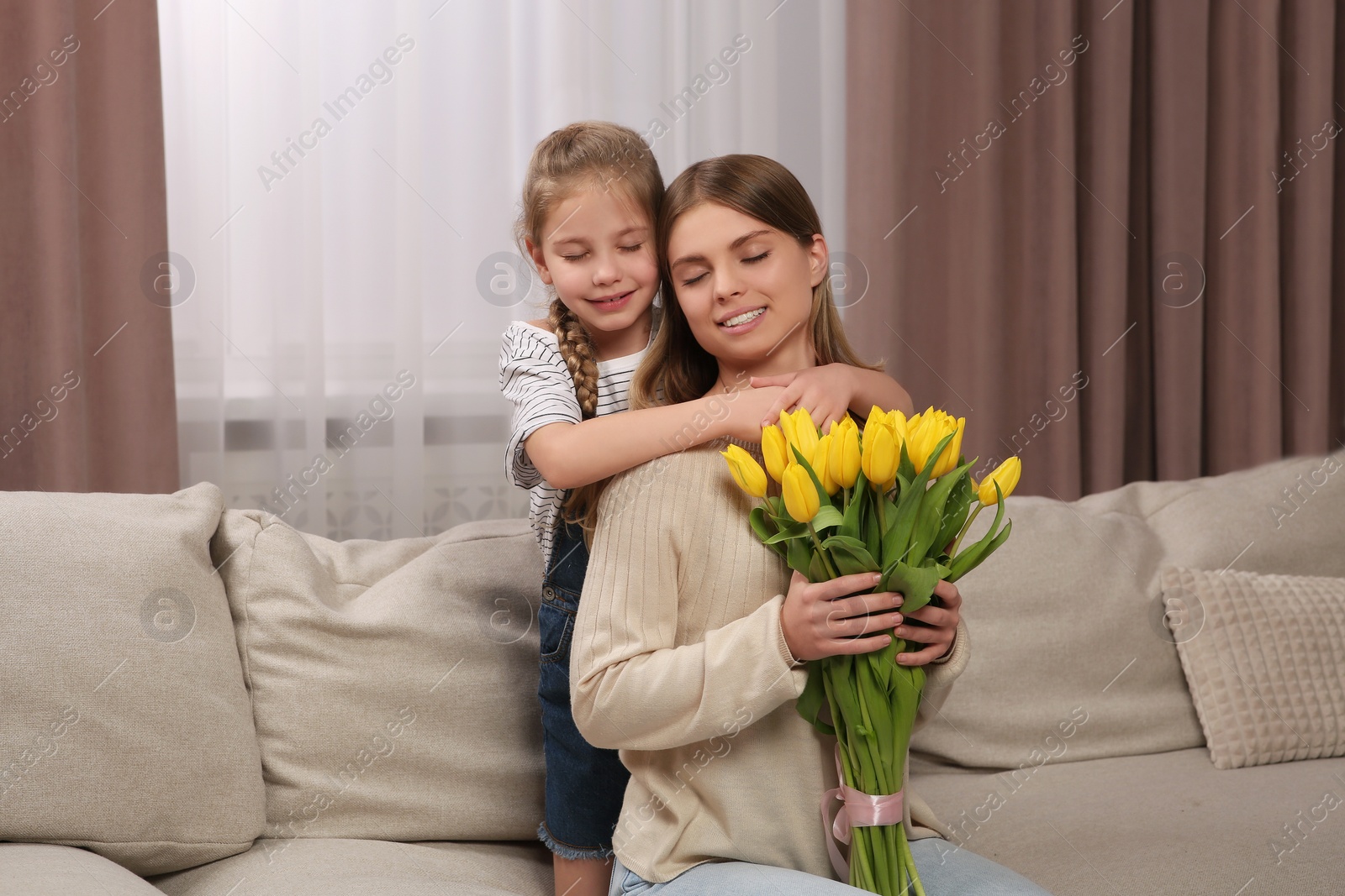 Photo of Little daughter congratulating mom with bouquet of yellow tulips at home. Happy Mother's Day