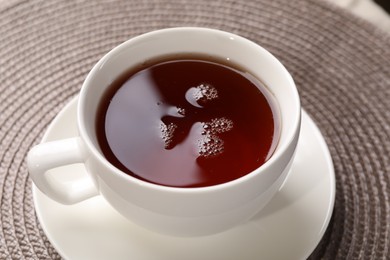 Aromatic tea in cup on mat, closeup