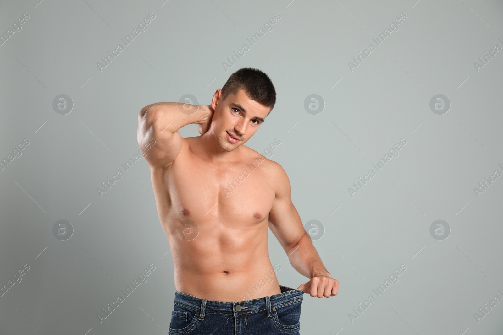 Photo of Young man with slim body in old big size jeans on grey background