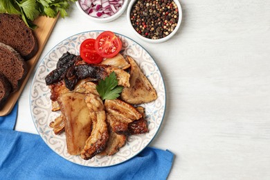 Photo of Tasty fried pork lard with parsley and tomatoes on white wooden table, flat lay. Space for text