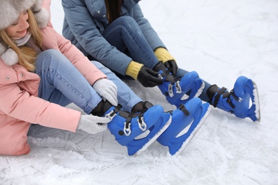 Photo of Happy women with figure skates sitting on ice rink outdoors