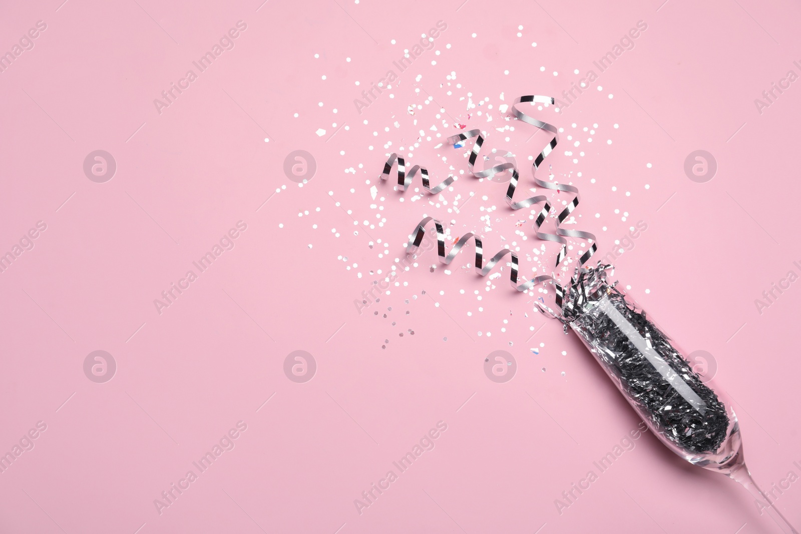 Photo of Glass and shiny confetti on pink background, flat lay. Space for text