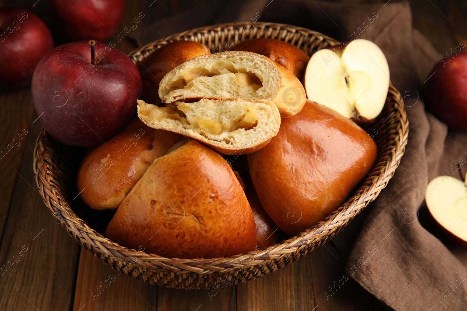 Photo of Delicious baked apple pirozhki in wicker basket and fruits on wooden table