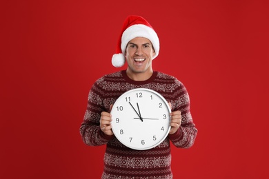 Photo of Man in Santa hat with clock on red background. Christmas countdown