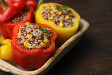 Photo of Quinoa stuffed bell peppers and basil in baking dish on wooden table, closeup