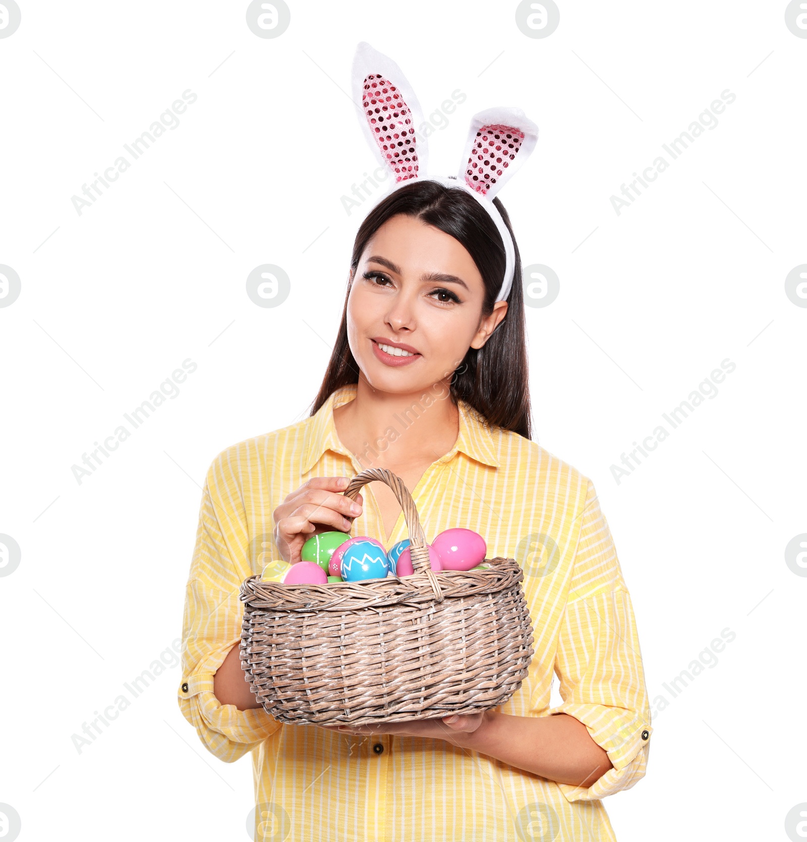 Photo of Beautiful woman in bunny ears headband holding basket with Easter eggs on white background