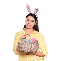 Photo of Beautiful woman in bunny ears headband holding basket with Easter eggs on white background