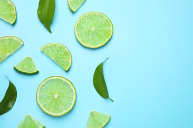 Photo of Juicy fresh lime slices and green leaves on light blue background, flat lay. Space for text