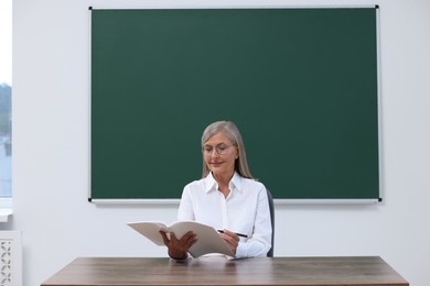 Professor with notebook and pen sitting at desk in classroom