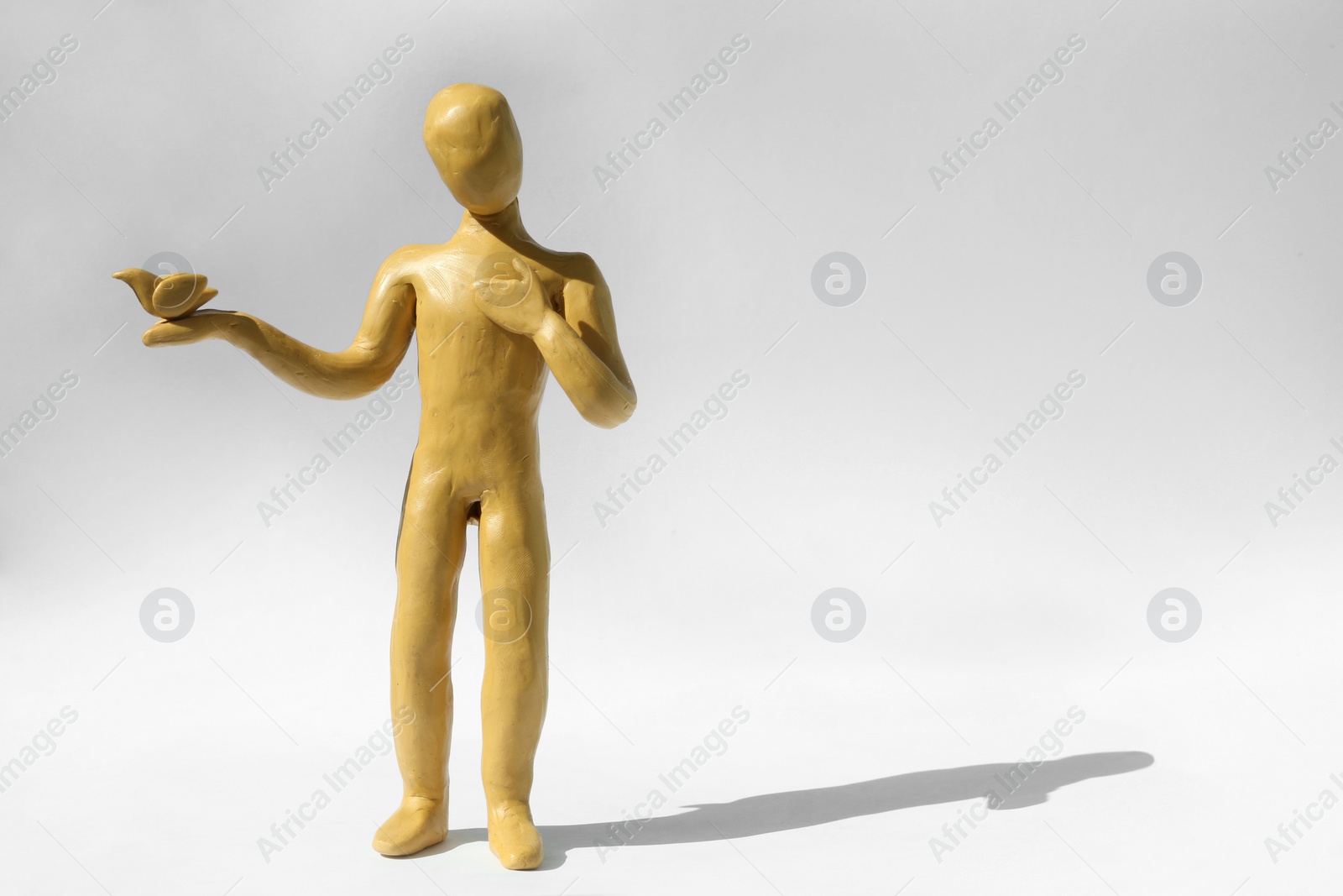 Photo of Yellow plasticine human figure with dove on white background, space for text