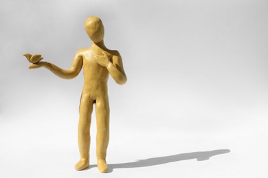 Photo of Yellow plasticine human figure with dove on white background, space for text