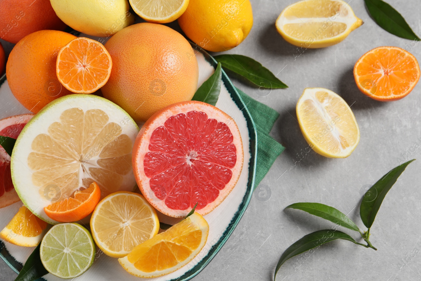 Photo of Different citrus fruits with fresh leaves on light grey table, flat lay