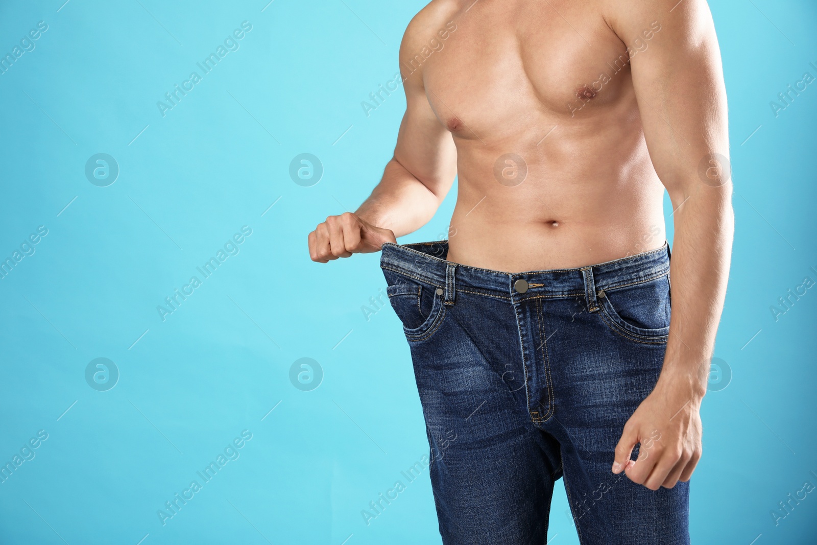 Photo of Young man with slim body in old big size jeans on light blue background, closeup view. Space for text