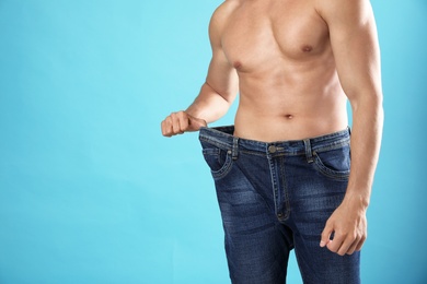 Young man with slim body in old big size jeans on light blue background, closeup view. Space for text