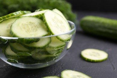 Photo of Cut cucumber in glass bowl on dark gray textured table, closeup