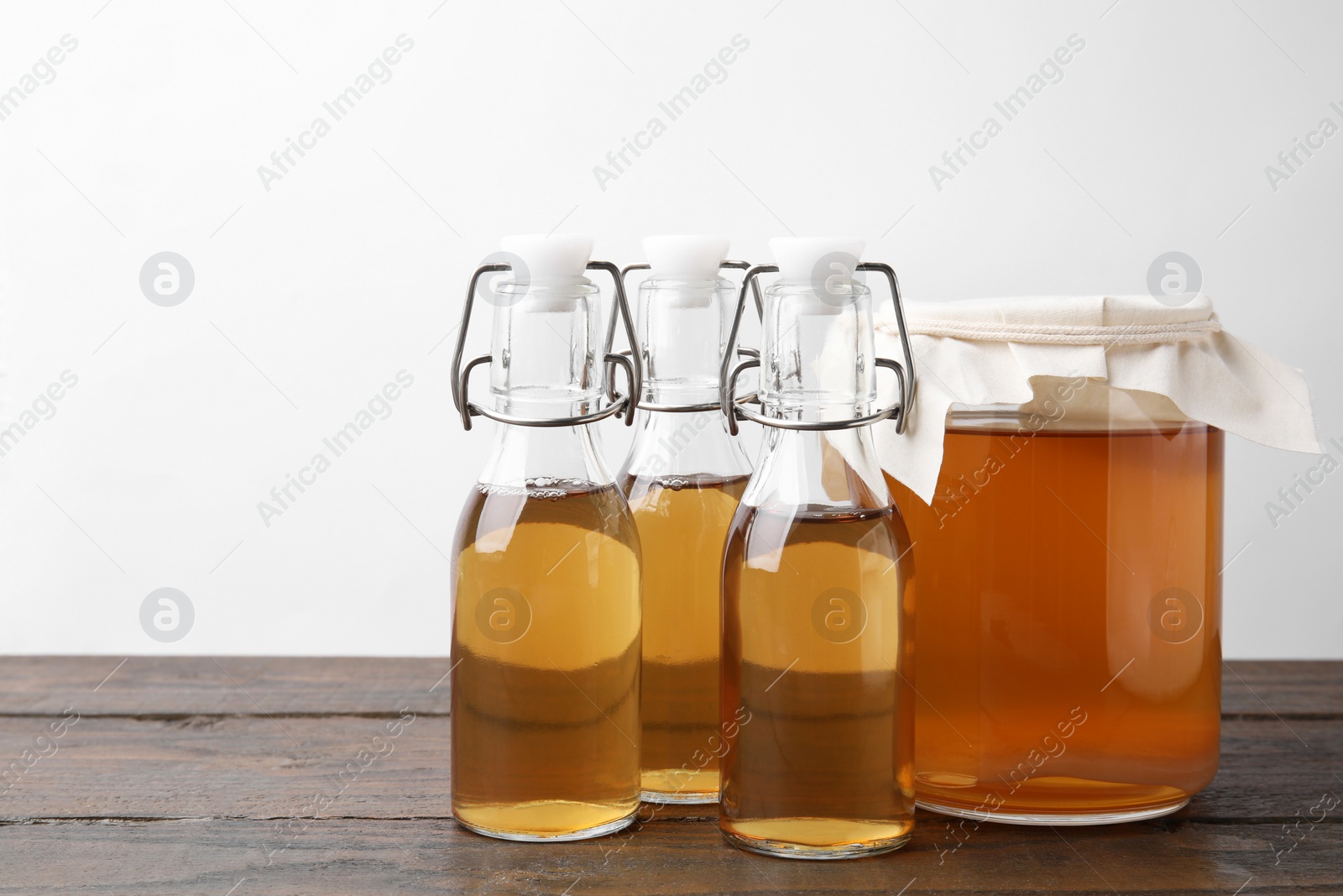 Photo of Homemade fermented kombucha in glass jar and bottles on wooden table. Space for text