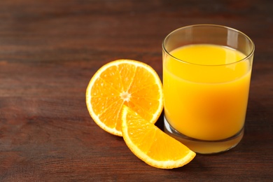 Photo of Glass of orange juice and fresh fruits on wooden table, closeup