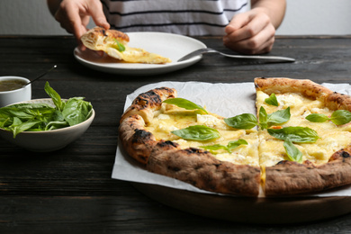 Photo of Woman having lunch at wooden table, focus on delicious cheese pizza