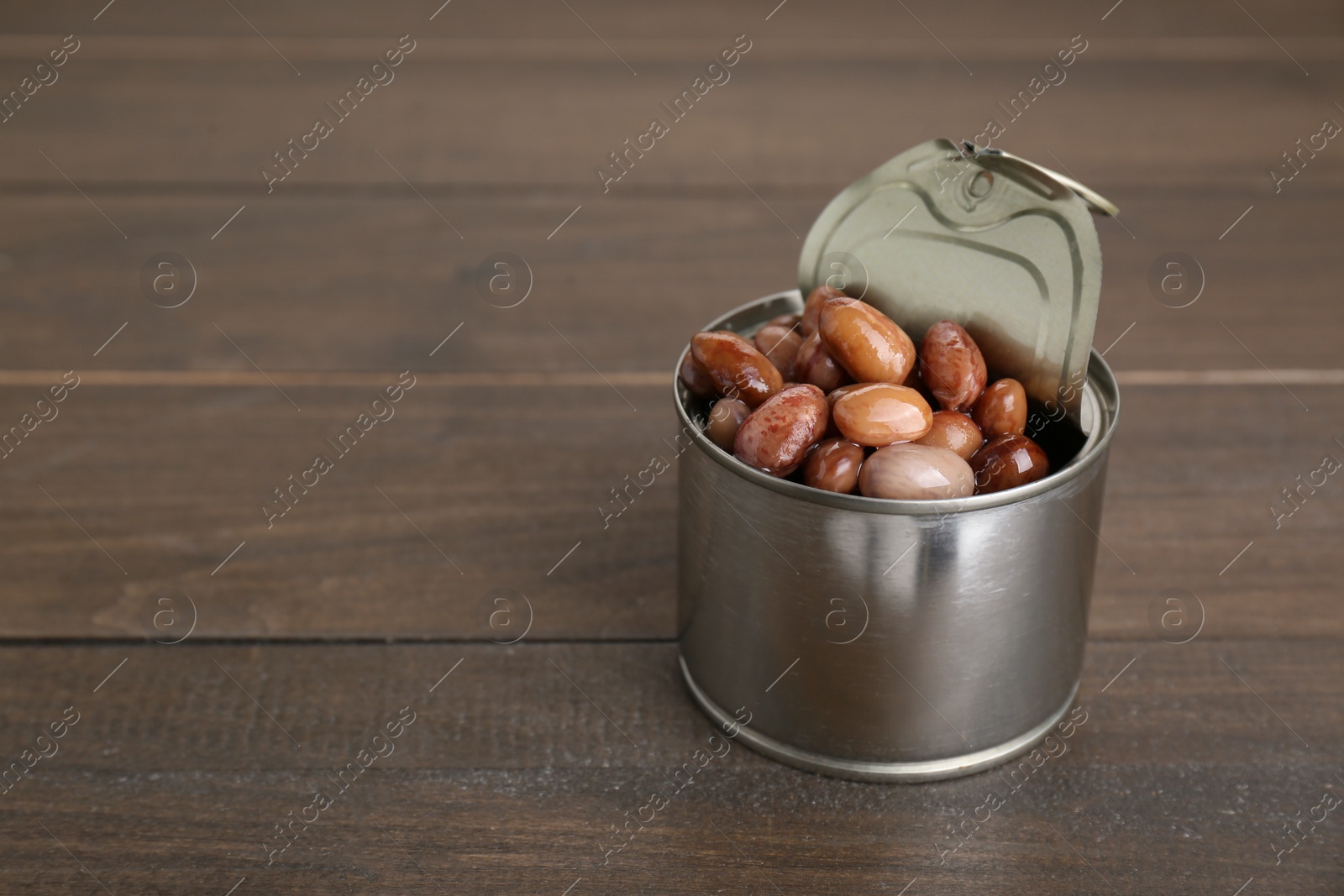 Photo of Tin can with kidney beans on wooden table, space for text