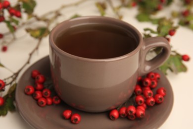 Photo of Aromatic hawthorn tea in cup and berries on beige table, closeup