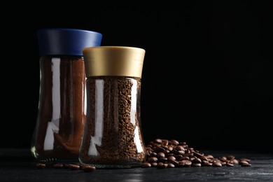 Photo of Glass jars with aromatic instant and ground coffee near beans on black wooden table. Space for text