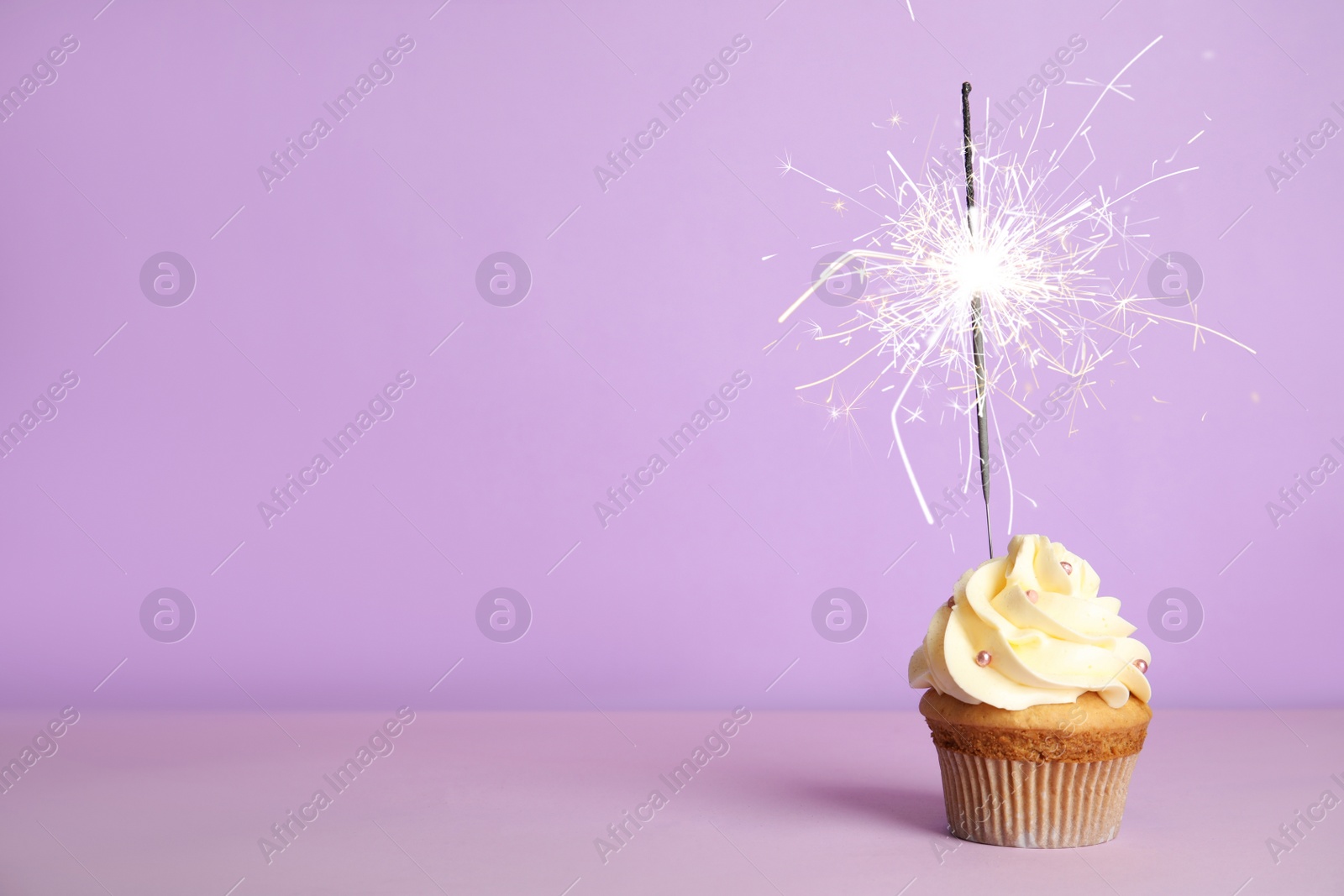 Image of Birthday cupcake with sparkler on violet background. Space for text