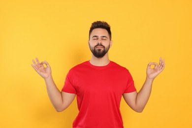 Photo of Young man meditating on yellow background. Zen concept