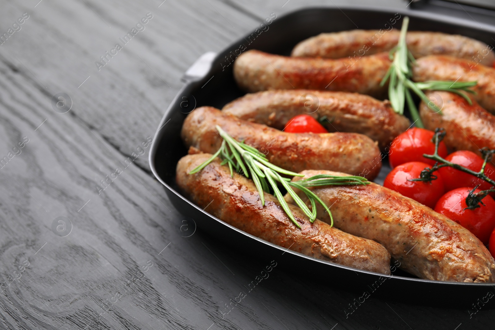 Photo of Pan with tasty homemade sausages, rosemary and tomatoes on grey wooden table, closeup. Space for text