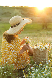 Photo of Woman with straw hat and handbag full of chamomiles resting in meadow