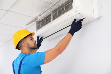 Photo of Professional technician maintaining modern air conditioner indoors