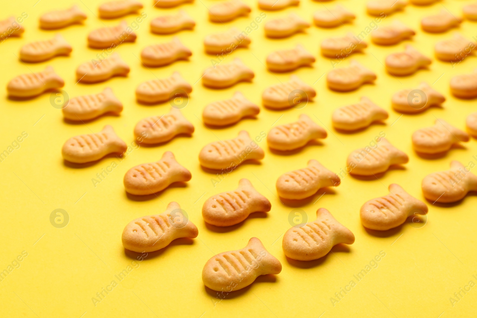 Photo of Delicious goldfish crackers on yellow background, closeup