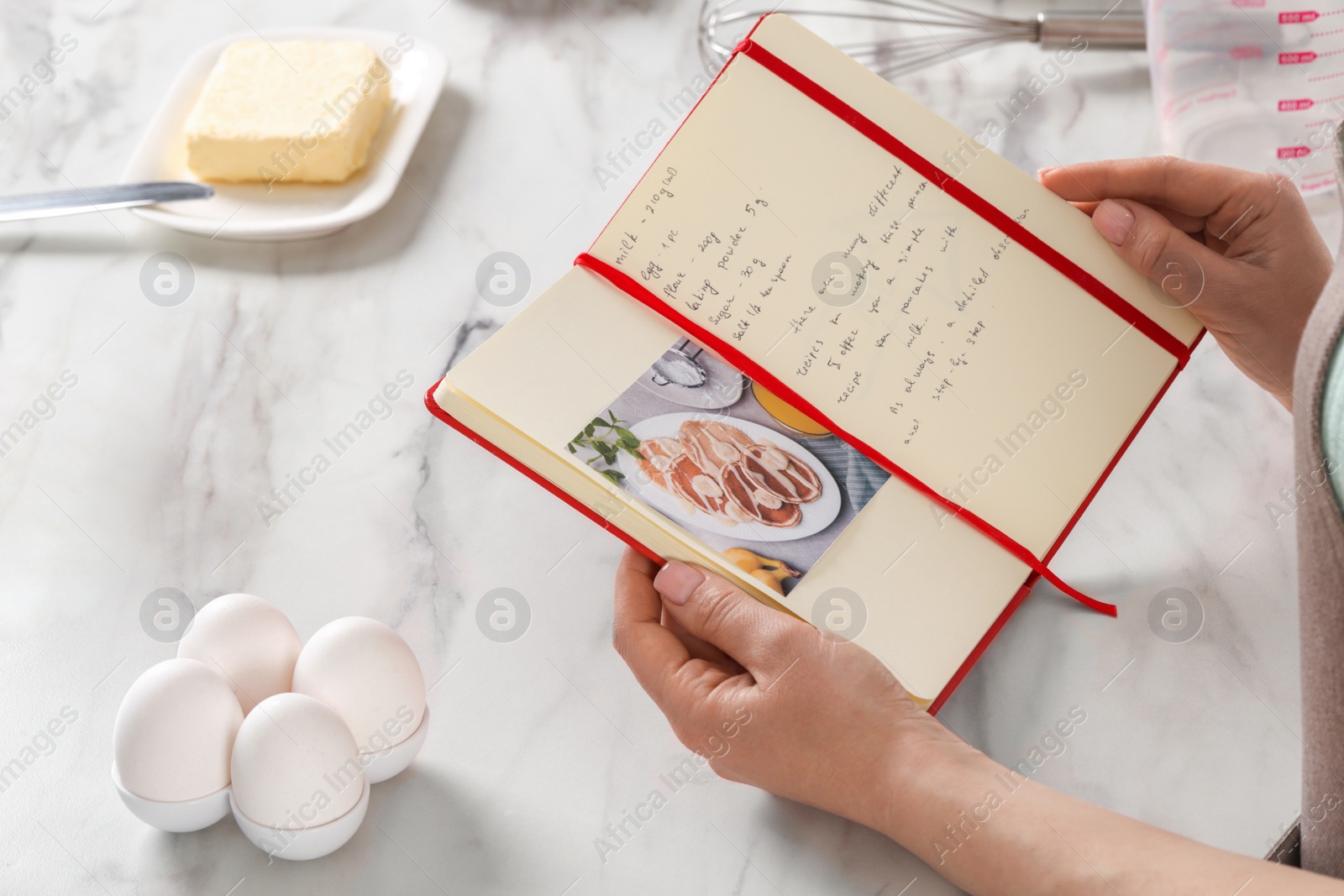 Photo of Woman with recipe book at white marble table in kitchen, closeup