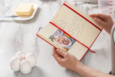 Woman with recipe book at white marble table in kitchen, closeup