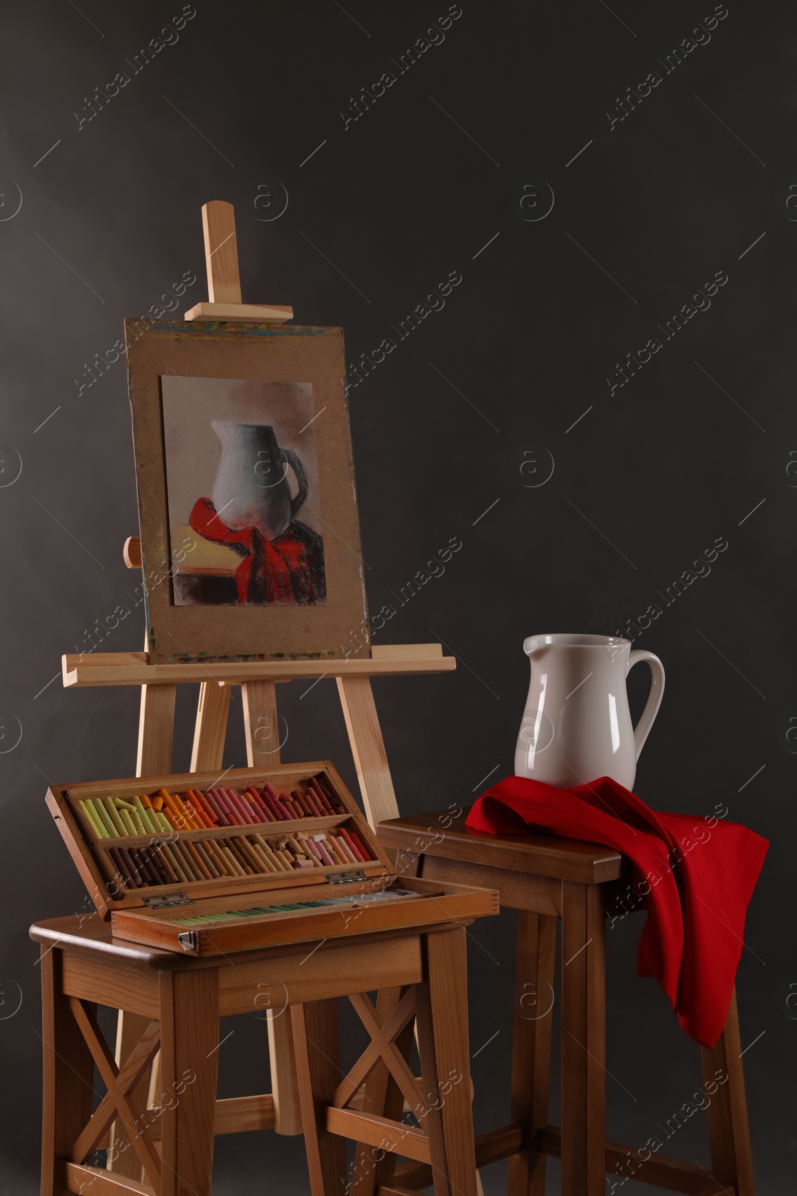 Photo of Artist's workplace with easel, drawing and soft pastels against black background