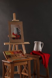 Photo of Artist's workplace with easel, drawing and soft pastels against black background