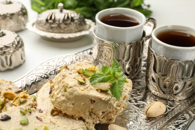 Photo of Tasty halva with pistachios and mint served on white table, closeup