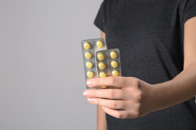 Photo of Woman holding pills in blister packs on gray background, closeup. Space for text