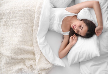 Young beautiful woman waking up after sleeping in bed at home, top view