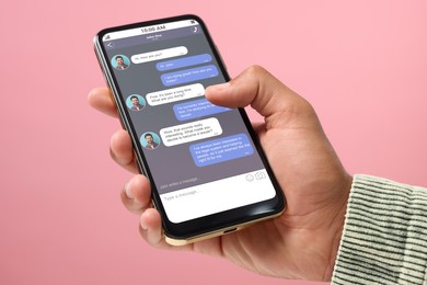 Man texting with friend using messaging application on smartphone against pink background, closeup