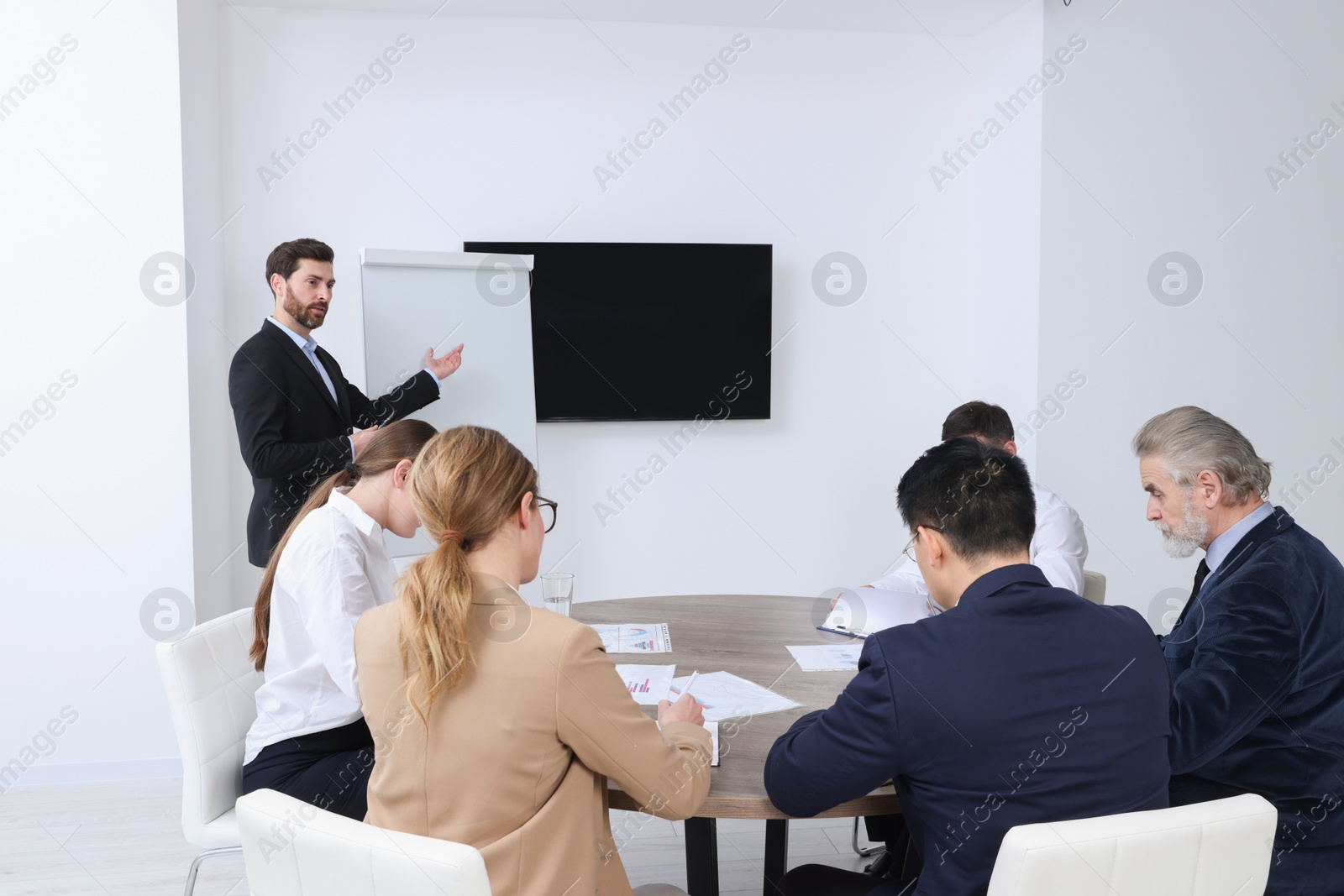 Photo of Business conference. Group of people listening to speaker report near tv screen in meeting room