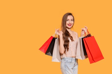 Photo of Stylish young woman with shopping bags on orange background, space for text
