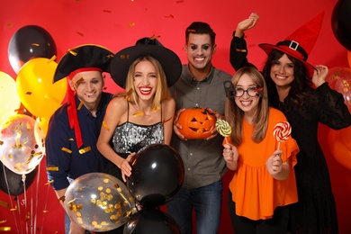 Photo of Happy friends in costumes with Halloween party accessories on red background