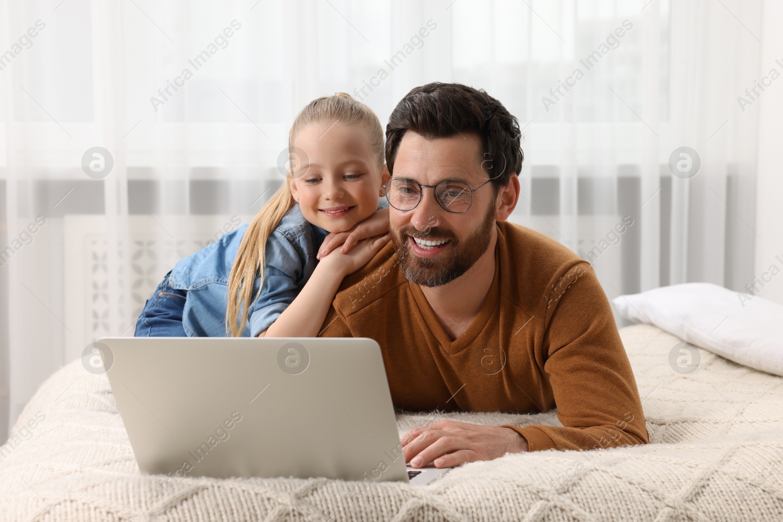 Photo of Happy man and his daughter with laptop on bed at home