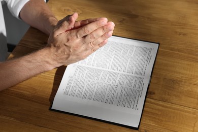 Photo of Man with Bible praying at wooden table, closeup