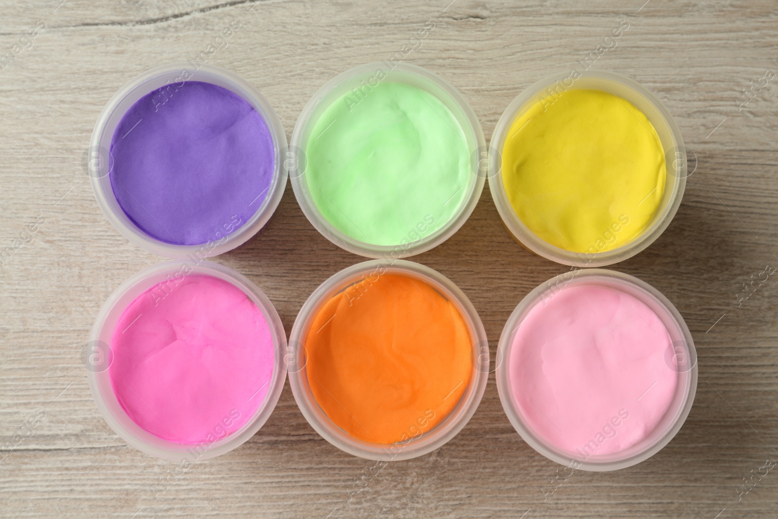 Photo of Plastic containers with colorful play dough on white wooden background, flat lay