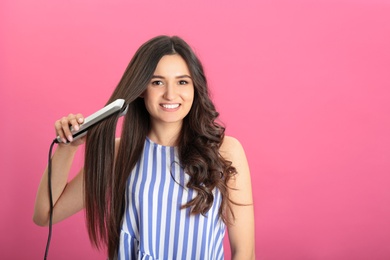 Photo of Young woman using hair iron on pink background, space for text